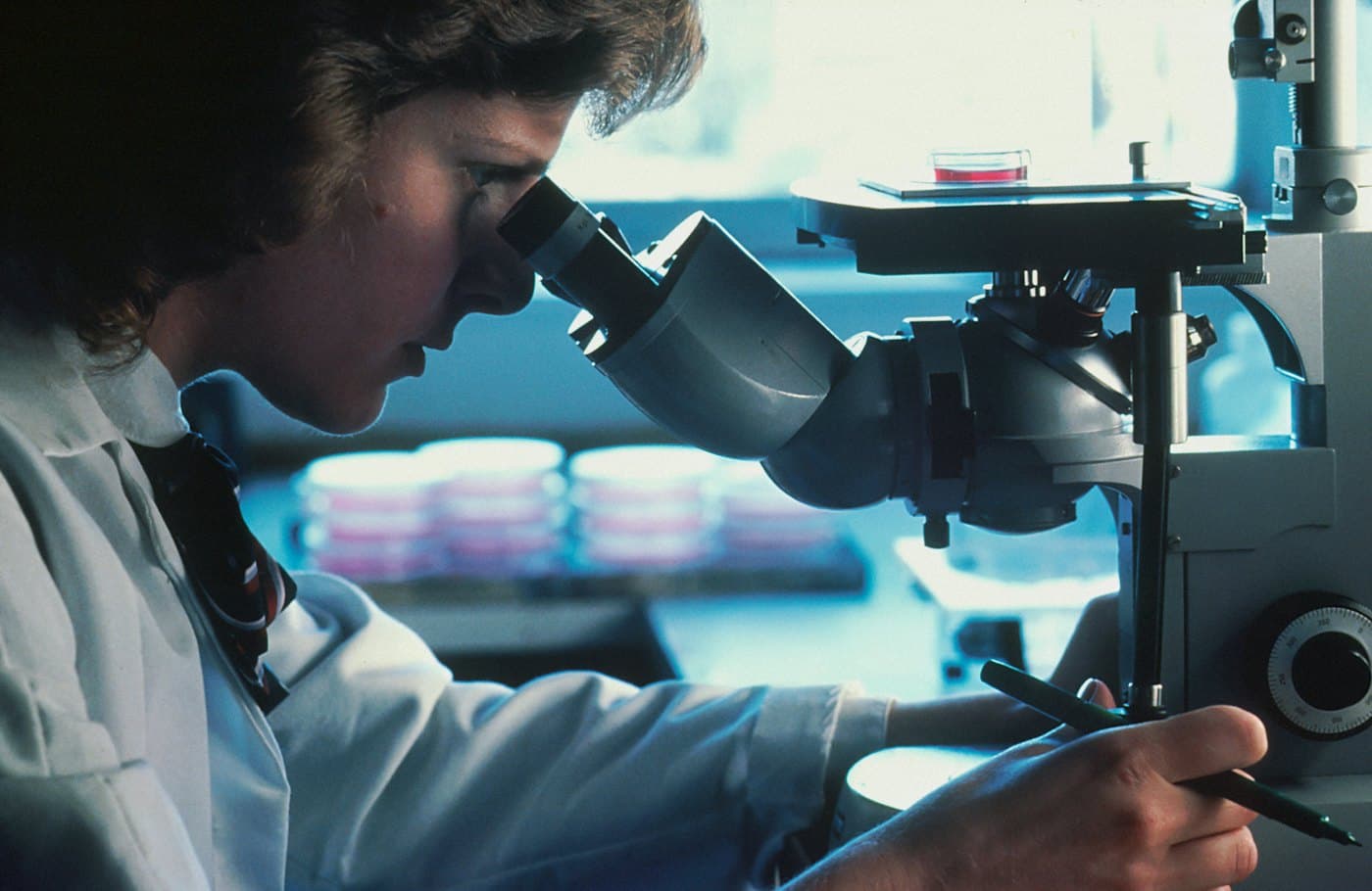 Researcher in a lab coat looking through a microscope